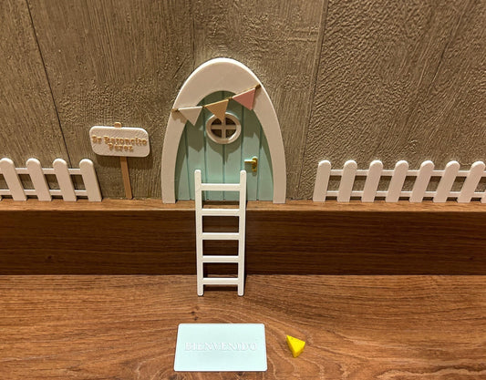 Kit mágico del Ratoncito Pérez con puerta en miniatura, escalera, valla, cartel de bienvenida y queso, creando un escenario encantador en 3D sobre una superficie de madera.